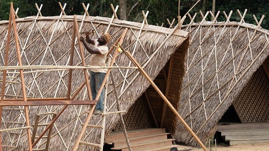A local builder constructing a hut with timber and thatch in Cameroon