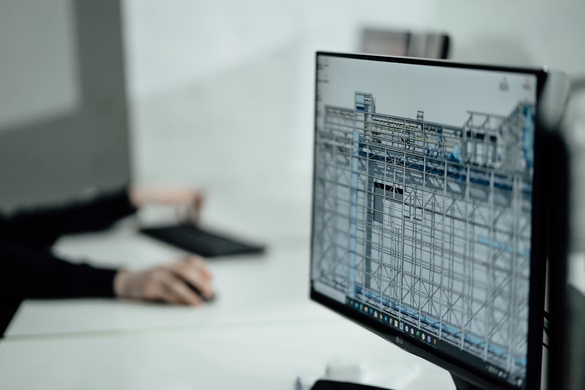 A Revit 3D model on a desktop monitor with a person typing on a keyboard in the background