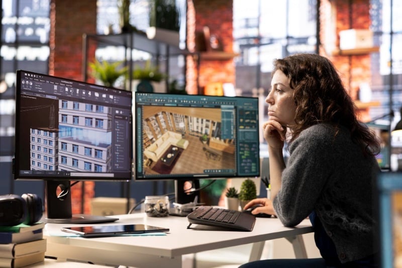 A designer using a dual-monitor setup to work on a 3D rendering project.