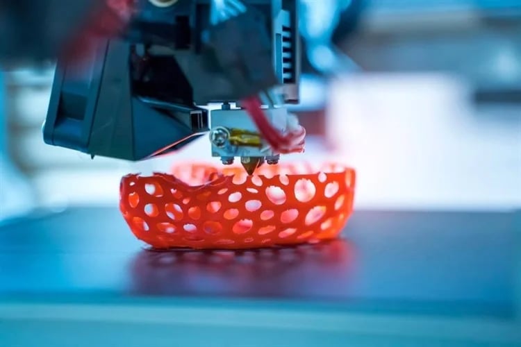 A nozzle 3D printing an orange thermoplastic material into a non-uniform lattice