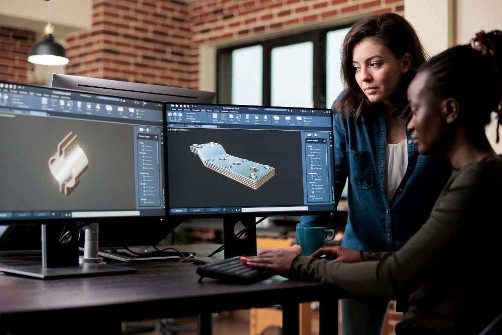 acade designers working on a computer-aided design program, reviewing a model of a mechanical part.