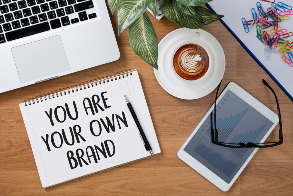 Image of a laptop, tablet, a coffee and a notebook with ‘You are your own brand’ written’
